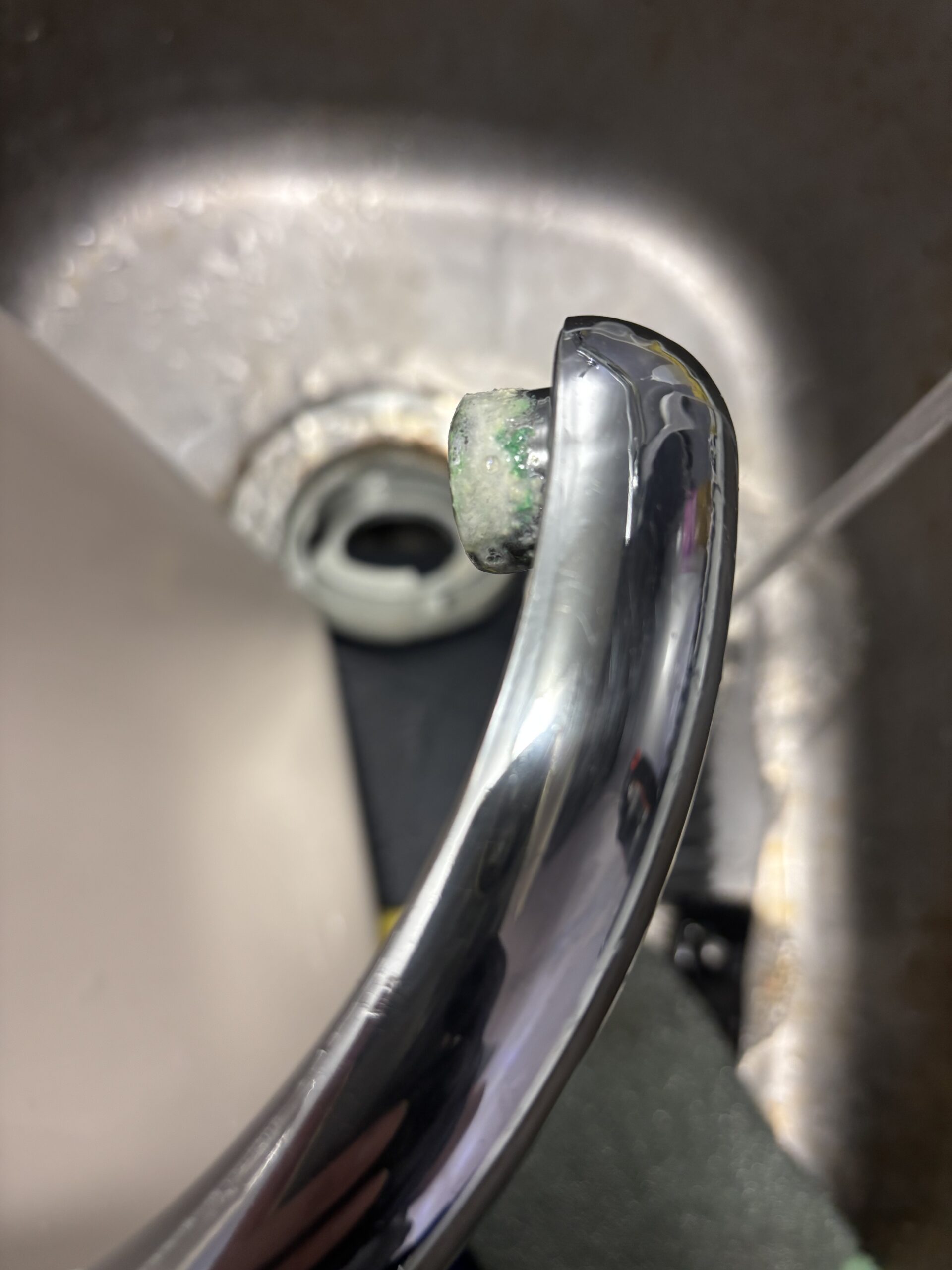 清掃前のトイレタンクの手洗い金具。吐水口の周囲に固まった付着物が見られる