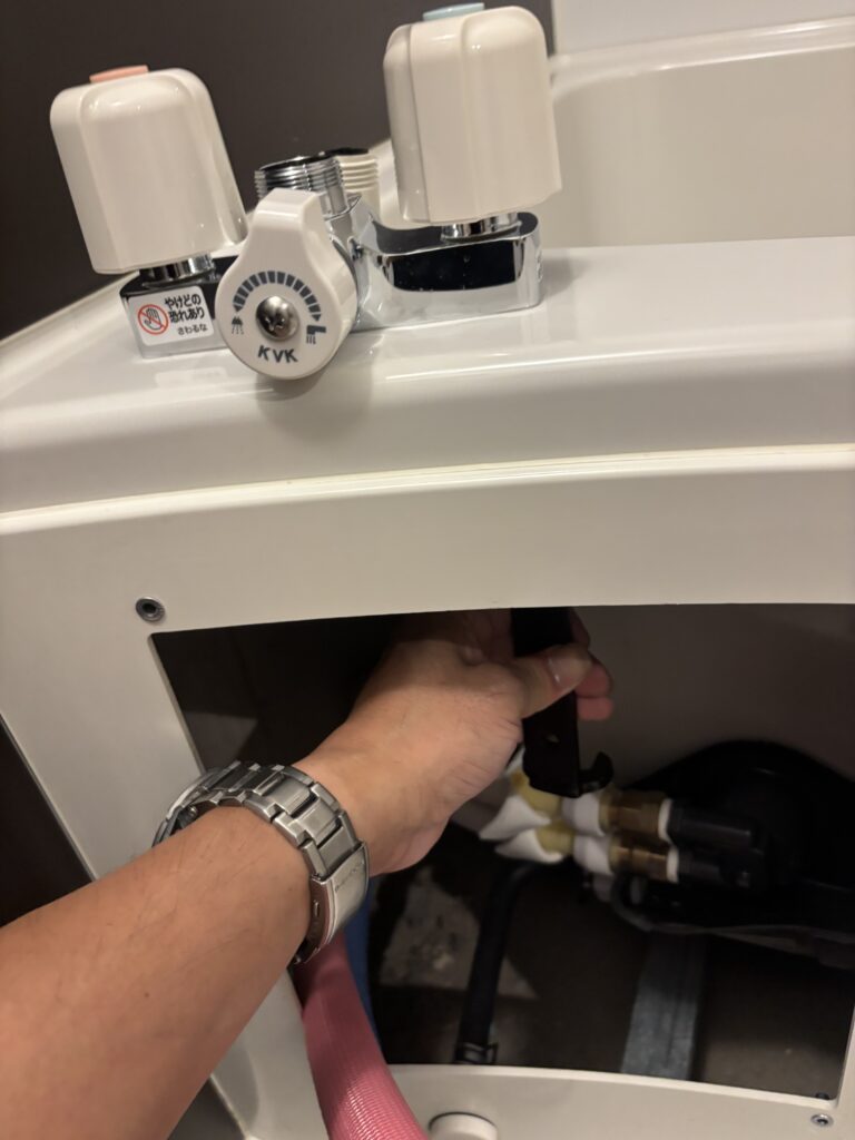 浴槽の台付き混合水栓の交換作業中。点検口から内側に手と工具を入れて作業している様子