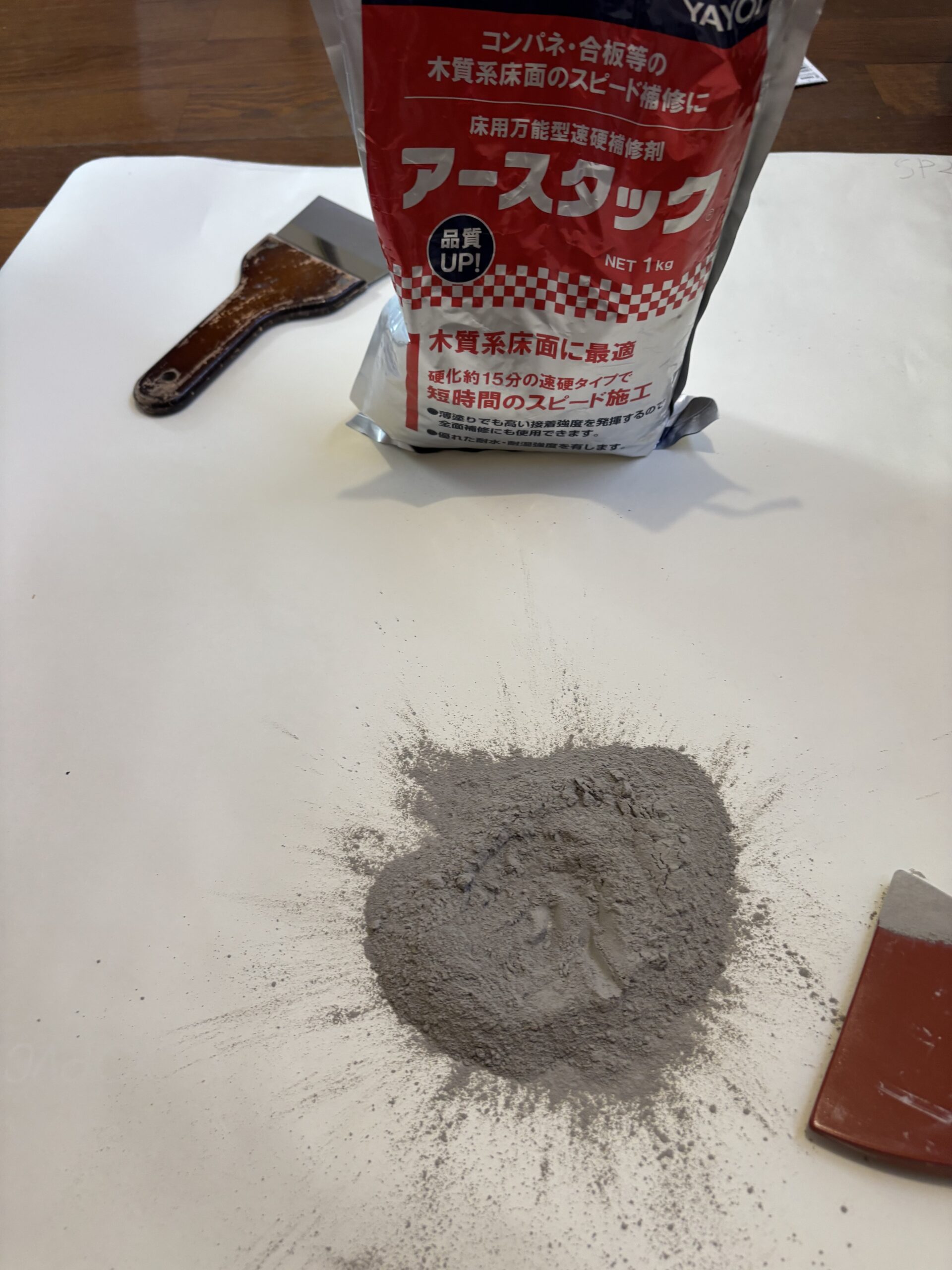 床の補修に使用したパテの材料とヘラ。袋にはアースタックの表示がある